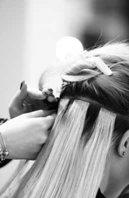 Professional hairdresser making hair extensions for blonde girl in a beauty salon